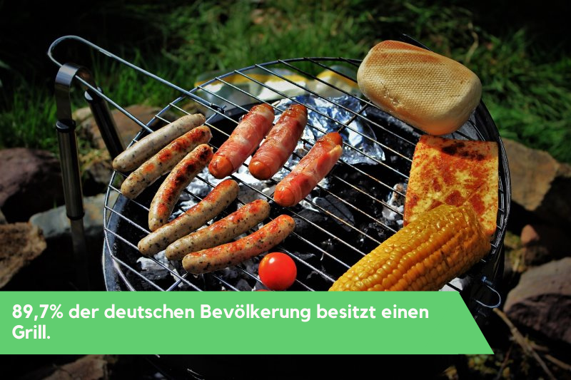 Auf einem Grill liegen Mais, Bratwürstchen, Brot, Tofu und eine Tomate