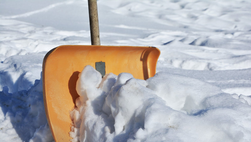 Orangefarbene Schneeschaufel im Schnee Schnee mit der Schneeschaufel schippen
