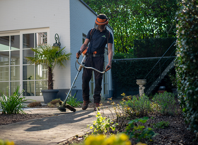 Mann mit Freischneider und Schutzkleidung im Garten Mann mit Freischneider und Schutzkleidung im Garten